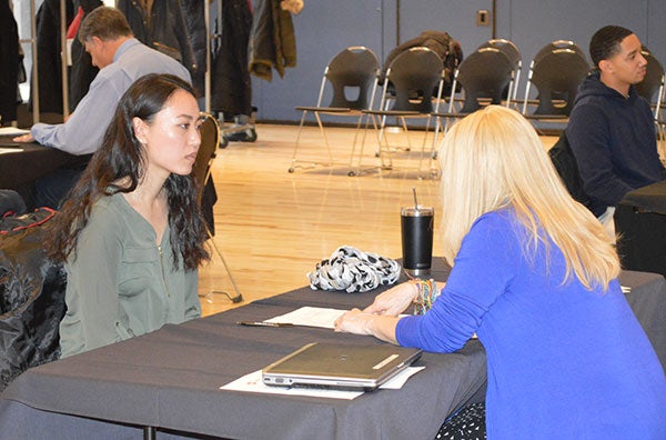 A woman is still at a table pointing to some papers and talking with another woman sitting across from her.