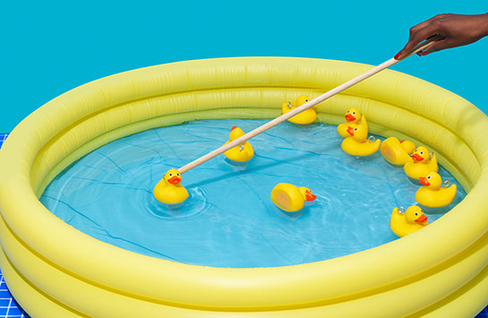 A person using a stick to push around rubber ducks in an inflatable pool