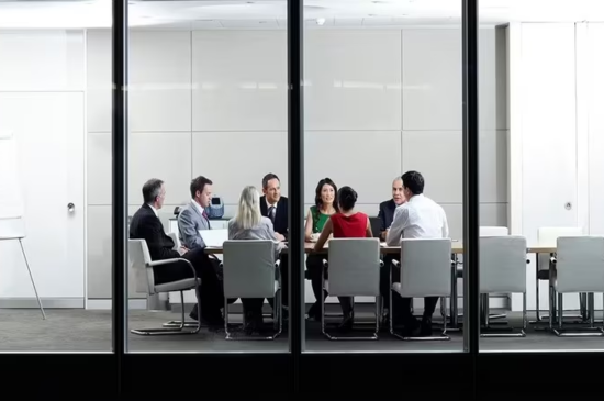 Faculty around a conference table which can be seen through a window.