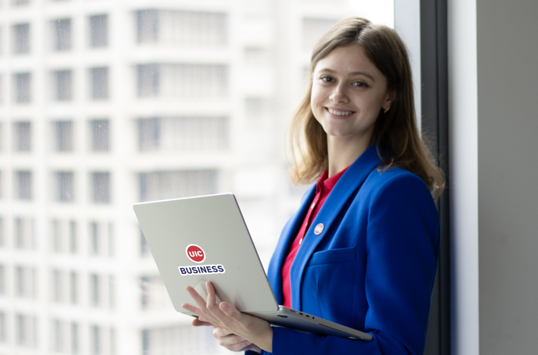 UIC Business MS Marketing Student on laptop by a window overlooking campus.